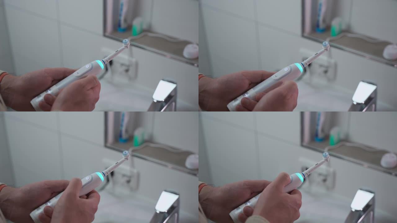 男人的手在浴室背景下打开或关闭带有蓝光的声波白色牙刷。牙齿卫生和洁白的牙齿。电动牙刷。清洁口腔的电动