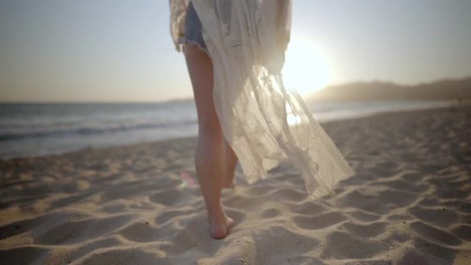 在墨西哥日落时，穿着白色海滩遮掩的女人沿着海滩散步。