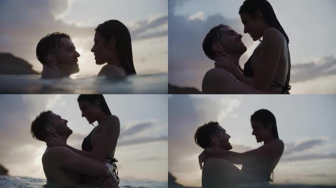 浪漫的异性恋夫妇在美丽的金色日落时在海里游泳。温柔地亲吻和拥抱