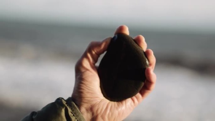 男子从海滩上拿着光滑的黑色卵石
