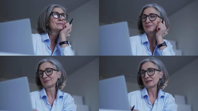 成熟的时尚公司秘书，白发和时尚的眼镜，正在考虑为客户提供正确的答案，在笔记本电脑上保持在线业务往来，