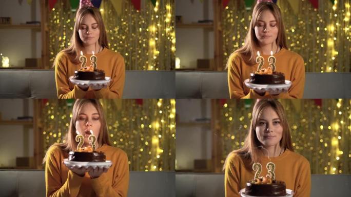 23岁生日。年轻女子在生日蛋糕上吹蜡烛23。女孩拿着蛋糕许愿