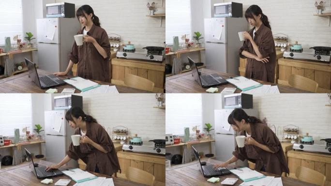 亚洲女性创意工作者一边喝茶，一边看着电脑，一边用胳膊放在胸前，一边在家里工作，一边弯腰在键盘上打字