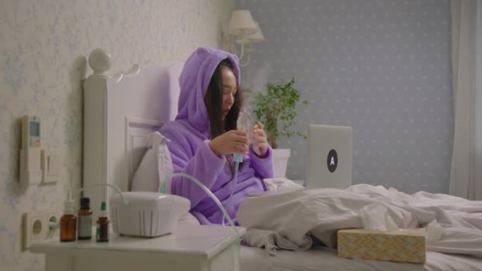 年轻的成年生病的亚洲妇女视频电话与医生握着吸入器在手中躺在床上。女性用药物吸入器治疗咳嗽。在家治疗流
