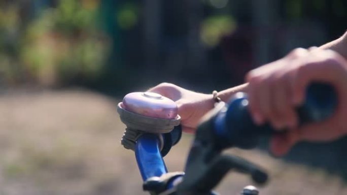 一个孩子的手在公园的自行车车把上敲响自行车铃的特写镜头。