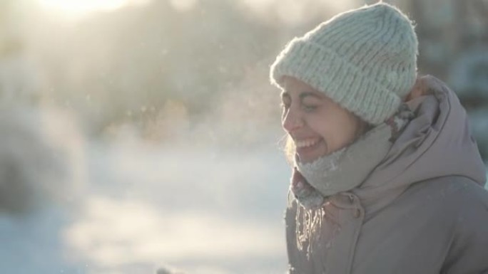 慢动作: 年轻女子吹雪。寒冷的冬日降雪后，有趣的女孩在冬季公园的手套上吹雪。快乐兴奋的女孩享受寒冷的