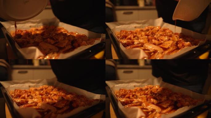 一个人的手将红色辣酱从碗里倒在托盘上的鸡翅上的特写镜头