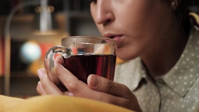 女人晚上喝茶，她的手把杯子放在嘴里。特写