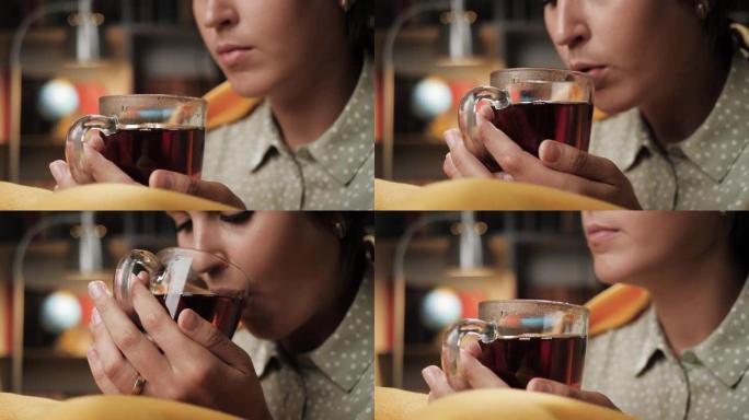 女人晚上喝茶，她的手把杯子放在嘴里。特写