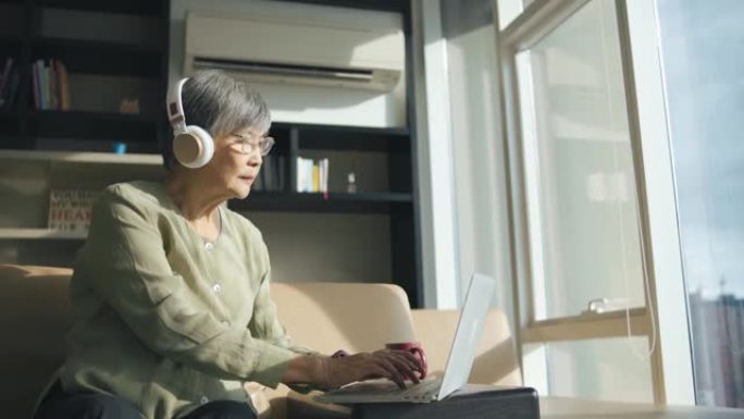 亚洲中国高级女性在城市公寓的客厅使用笔记本电脑电子学习听力