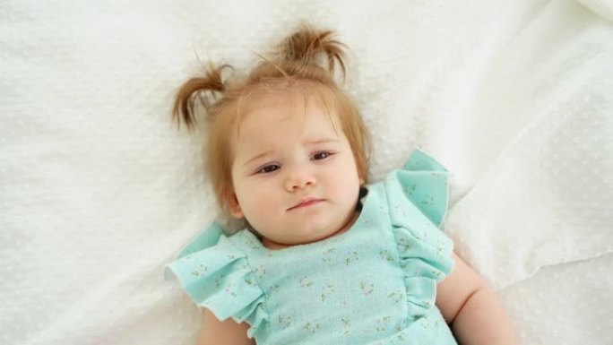 可爱的高加索女婴的特写肖像，辫子躺在床上看着相机。儿童商品广告。顶视图