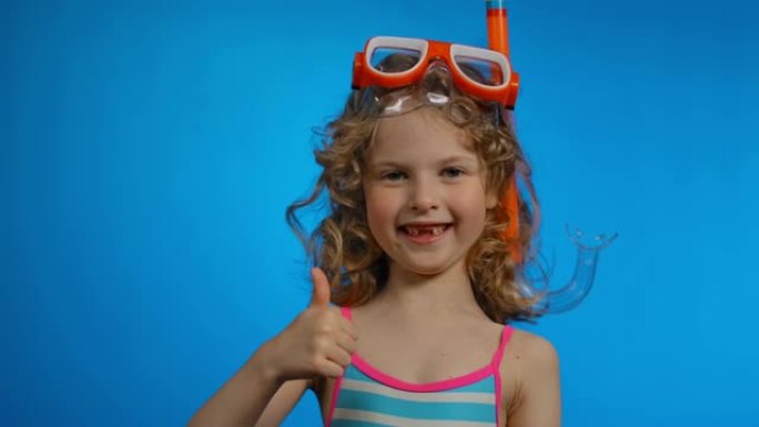 戴着游泳面具和通气管的可爱的卷发女孩在工作室里展示大拇指