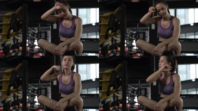 年轻的女运动员在健身房训练时坐在脸上擦汗。