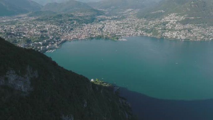 在夏季晴朗的天空中，飞越被群山环绕的湖泊，远处的卢加诺市