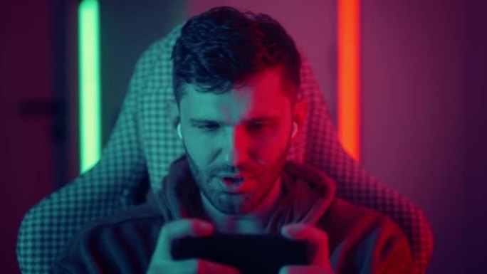 快乐的男人游戏玩家穿比赛玩视频游戏与智能手机彩色霓虹灯在客厅晚上现代房子。Esport流媒体游戏在线