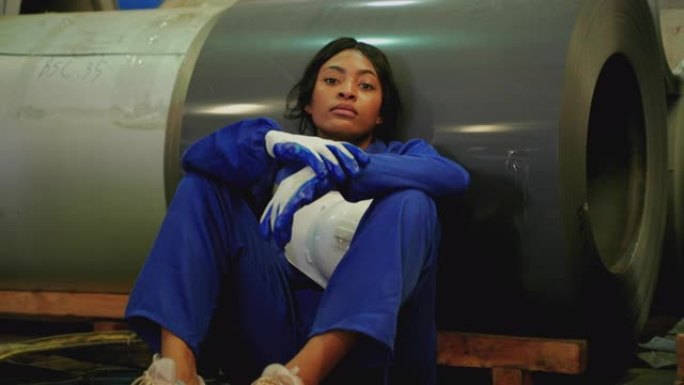 非裔美国女性仓库工人疲惫地坐在金属片厂和仓库内的仓储配送中心，压力观念，无聊，劳动