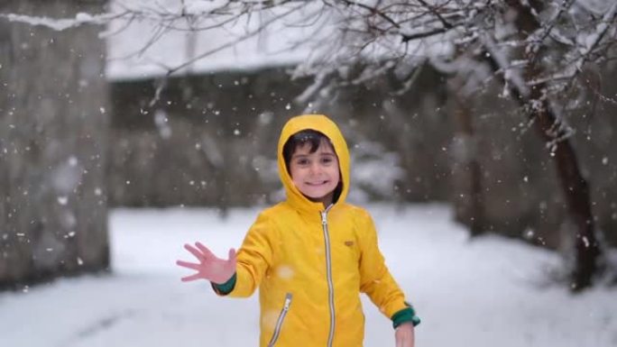 穿着黄色冬装的有趣小男孩在降雪时行走。孩子们的户外冬季活动。