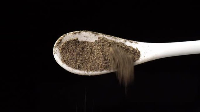 将汤匙上的黑胡椒粉倒在黑色背景上。用勺子干调味料。用于烹饪的香料和草药，胡椒粉