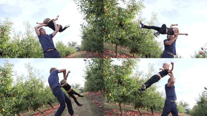 家庭娱乐父亲和小儿子在苹果树花园散步时在空中旋转一个孩子