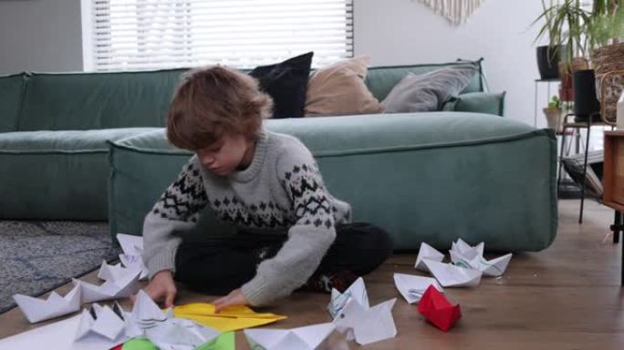 带着纸的小男孩在家制作一艘船。可爱的男孩在房间里折叠折纸船。