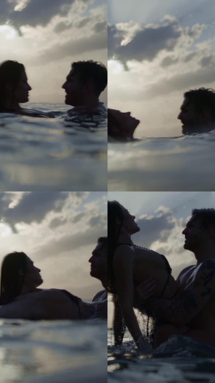 浪漫的异性恋夫妇在金色日落时在海里游泳。在水中播放和拥抱垂直视频