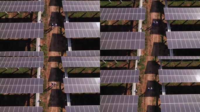 在太阳能电池板农场，电力，太阳产生的清洁能源之间沿着小线行走的工程师和技术人员的鸟瞰图