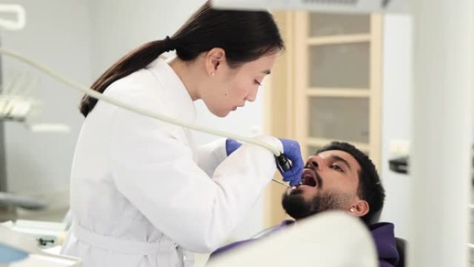 穿着白色制服的漂亮女性亚洲牙医，用钻头进行牙科检查和龋齿治疗