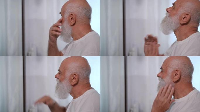 自信的老人在慢动作中触摸白胡子的侧视图特写，拇指向上看向远处。微笑着满足的白人男性退休人员早上在家欣