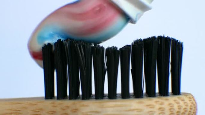 在白色背景上的木制牙刷上挤压多色牙膏。白牙概念