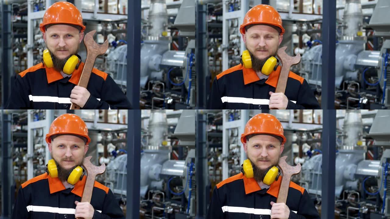 石油和天然气工业机械师的特写镜头站在戴着大扳手的头盔和耳机的压缩机上。天然气压缩和运输厂的石油工人的