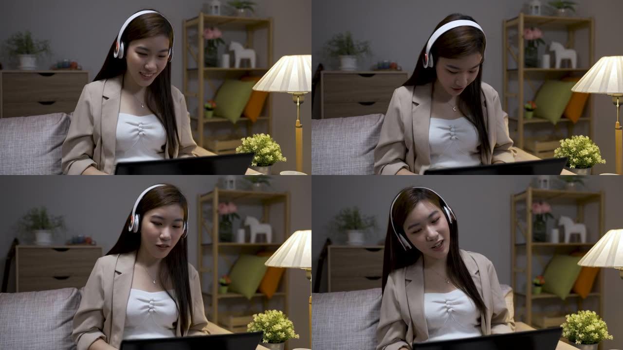 特写镜头，一个快乐的亚洲女商人晚上在客厅的沙发上用电脑工作时听耳机里的歌。