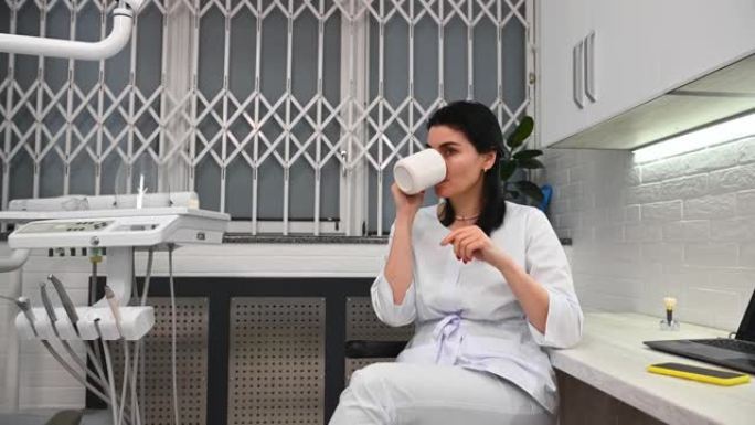 自信的白人女医生在辛苦工作一天后放松身心，在牙医办公室享用咖啡