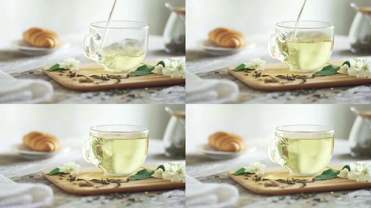绿色茉莉花茶在玻璃杯中流动。竹板上有茉莉花小枝的透明杯子