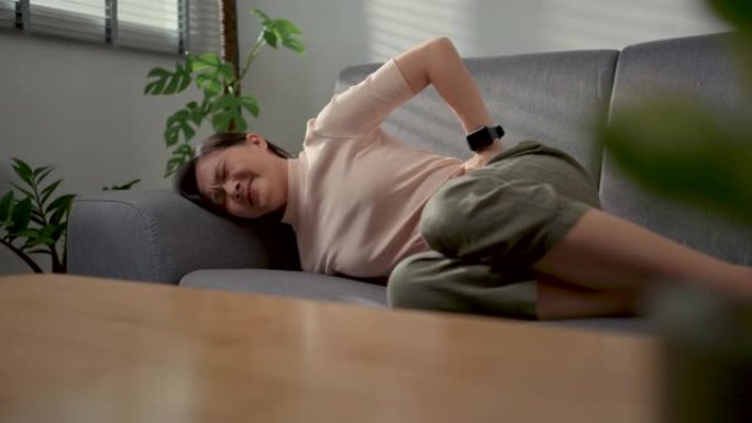 亚洲女人躺在家里客厅的沙发上胃痛。