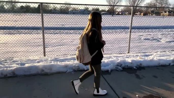 年轻漂亮的女孩在冬天走在链节围栏旁边的人行道上