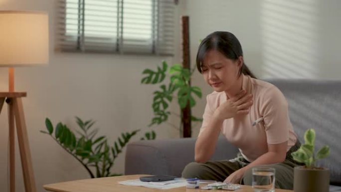亚洲妇女生病发烧，用温度计检查体温坐在家里客厅的沙发上。