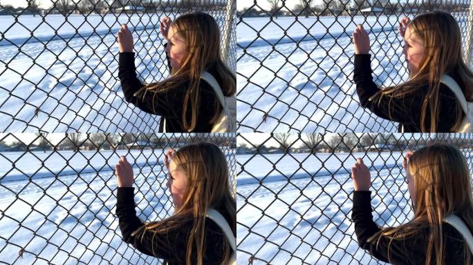 年轻女孩透过学校的铁丝网围栏