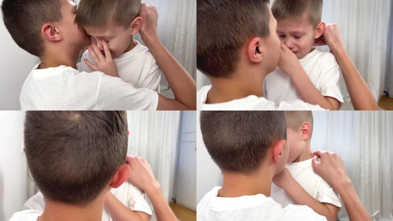 小男孩5岁哭他用手指摩擦眼睛哥哥12岁平静了他在耳朵里拥抱，看着他白色背景白色t恤关心家人不要哭亲爱