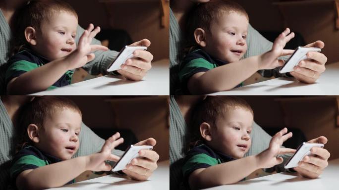 婴儿点击手机屏幕。女人的手握着手机，可爱的2-3岁的蓝眼睛孩子坐在母亲的怀里，在智能手机屏幕上轻拍手