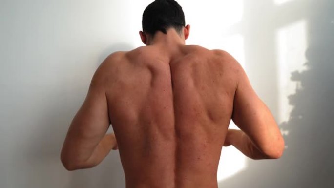 裸体肌肉男人揉捏他的背部，感觉他的脊椎和下背部疼痛。