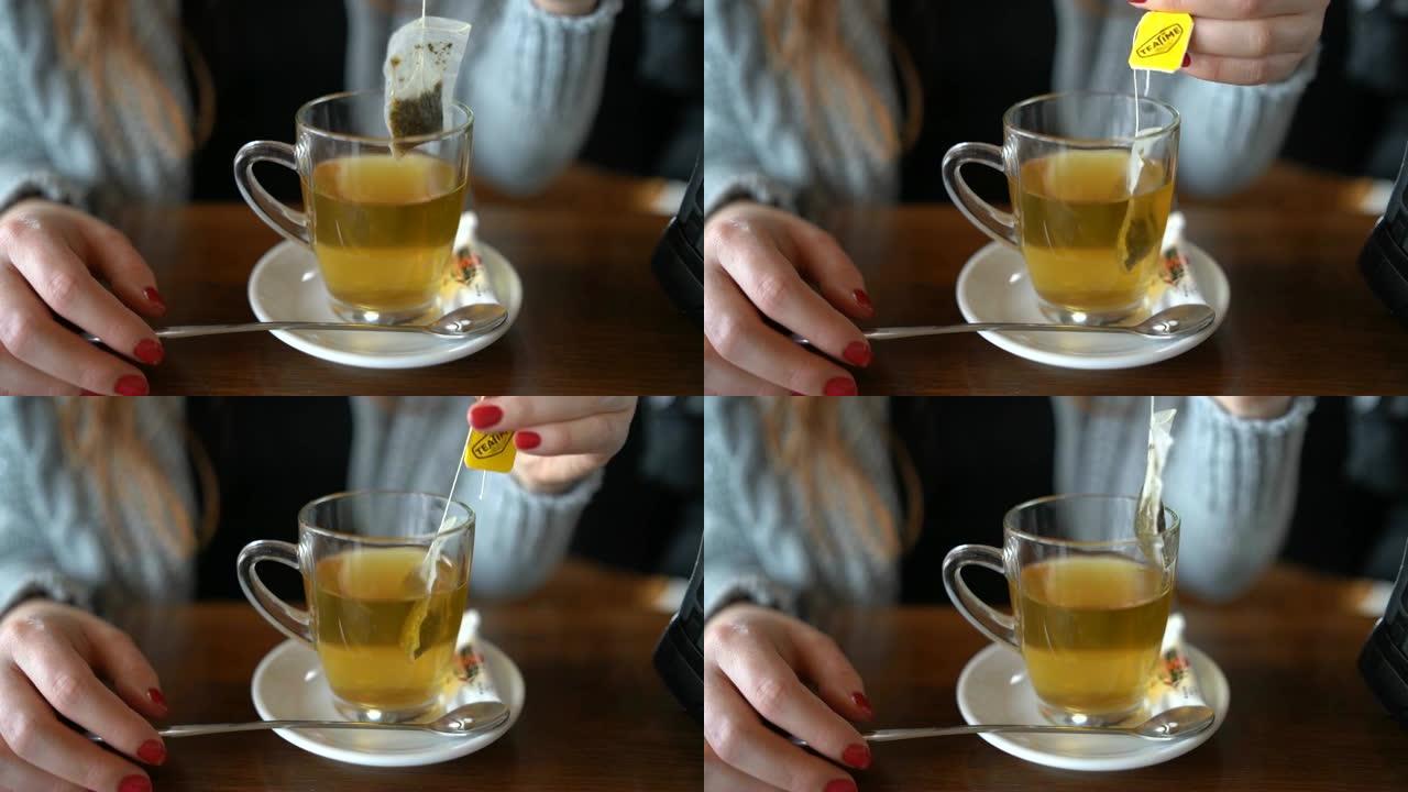 女人的手在咖啡馆的杯子里蘸茶袋