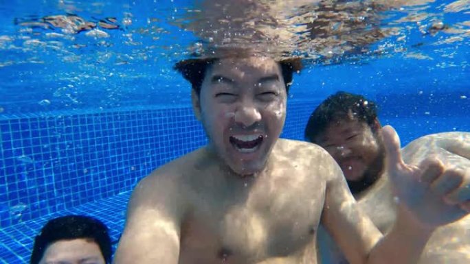 三个亚洲游客在度假胜地游泳池里一起在水下写博客，看着相机