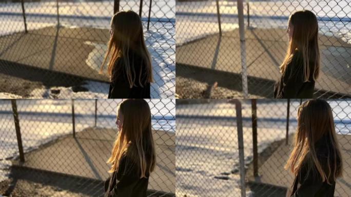 女孩在小学附近的铁丝网围栏旁行走