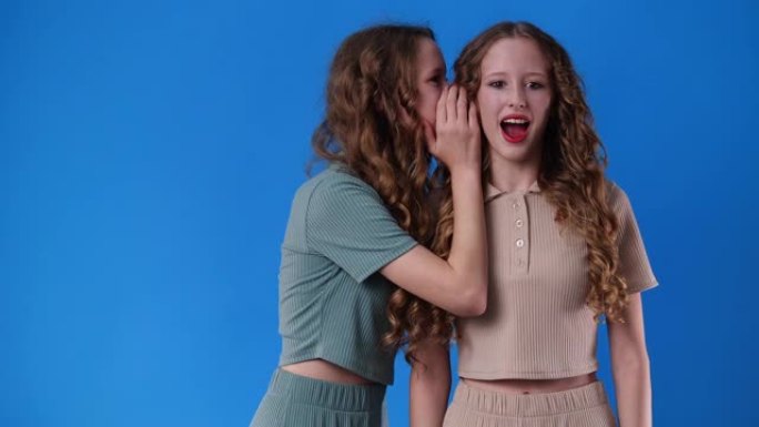4k慢动作视频，双胞胎女孩在蓝色背景上有一些秘密。