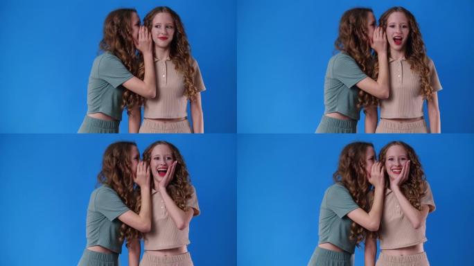4k慢动作视频，双胞胎女孩在蓝色背景上有一些秘密。