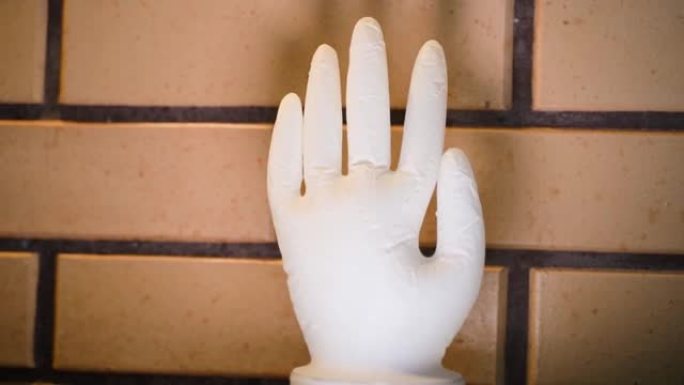发酵葡萄酒时用医用手套代替水封的特写镜头。膨胀的白色乳胶手套靠在咖啡色的装饰砖墙上。举手，平滑视差