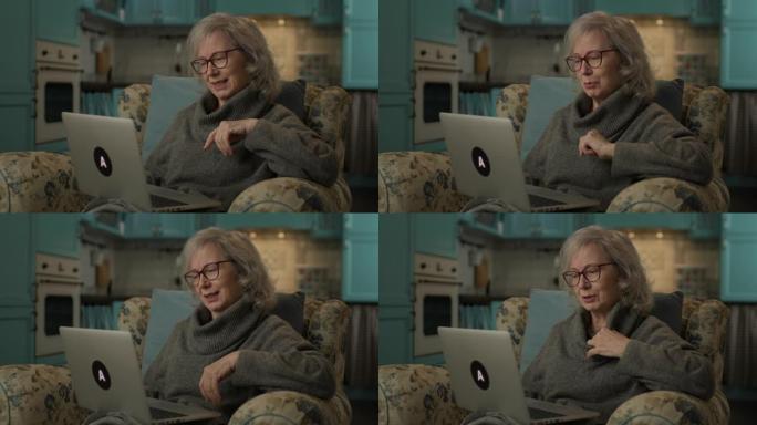 老年妇女在家视频通话。老年妇女坐在扶手椅上与笔记本电脑交谈。