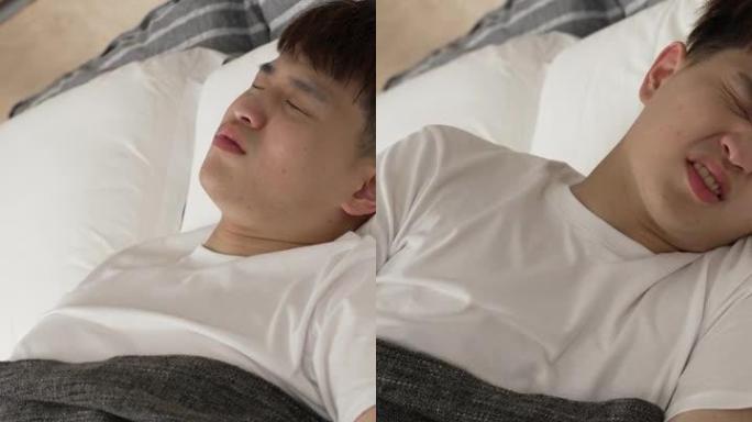 竖屏: 中国年轻男性早上在家里的卧室床上睡觉时，腹部突然疼痛，痛苦地呻吟着。