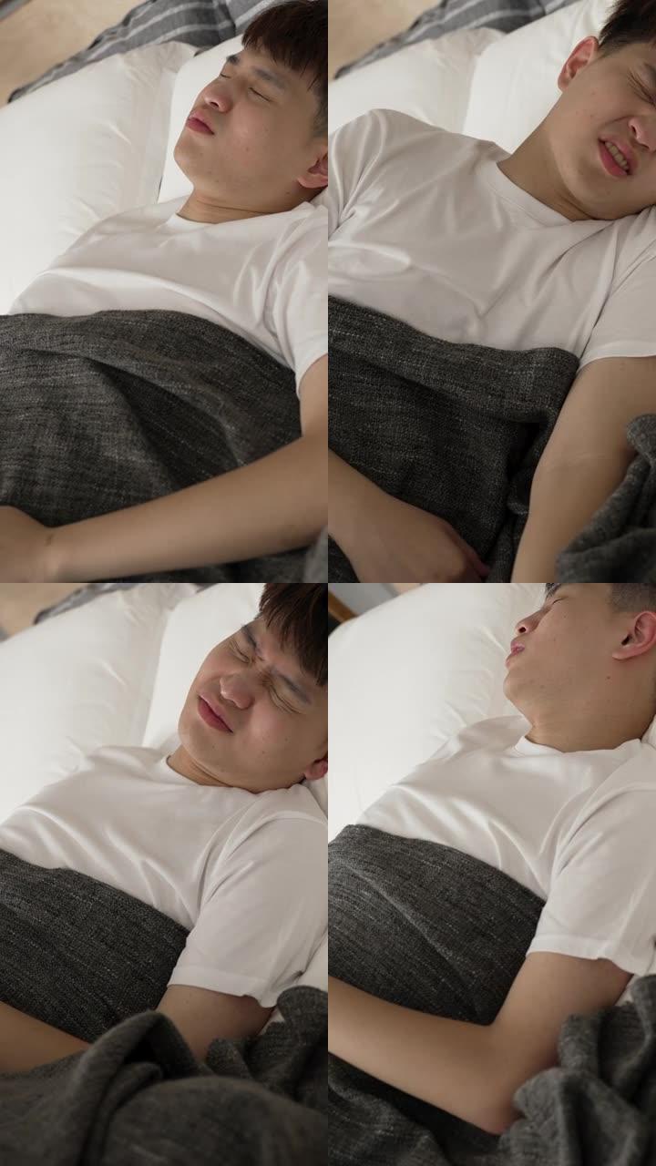 竖屏: 中国年轻男性早上在家里的卧室床上睡觉时，腹部突然疼痛，痛苦地呻吟着。