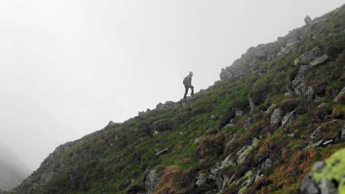 单人男徒步旅行者爬上罗马尼亚法加拉斯的落基山脉，背后笼罩着阴沉的雾